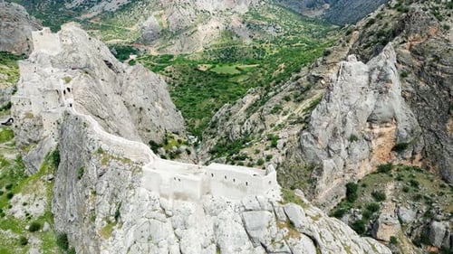 Drohnenaufnahme einer historischen Festung aus der Luft, die entlang dramatisch Bergklippen mit Blick auf eine Schlucht errichtet wurde