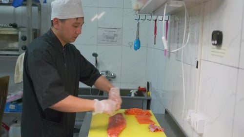 Skilled chef asian man in gloves filleting fresh salmon sea fish on a yellow cutting board