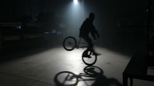 Young bmx rider performs daring stunts in a dark urban warehouse