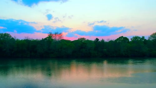 Drohne fliegt bei Sonnenuntergang auf dem Fluss mit buntem Himmel im Hintergrund. Aus der Luft vorwärts aufsteigend