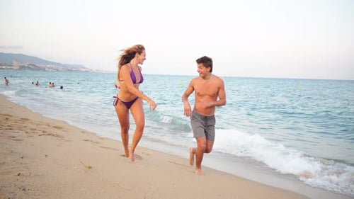 Joyful Young Couple Running Along the Sandy Beach During a Sunny Summer Day Filled with Laughter