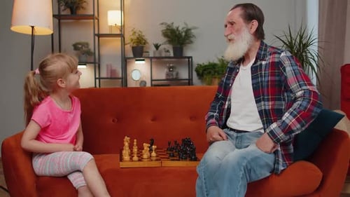 Smiling Senior Grandfather Playing Chess Board Game with Teen Granddaughter Child Girl Kid at Home