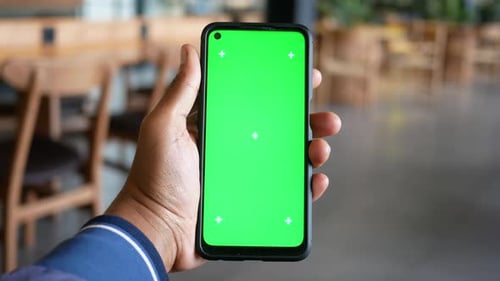 Hand Holding Smartphone with Green Screen in Modern Cafe Setting