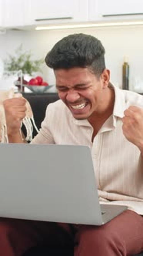 Man Cheering Success While Using Laptop at Home