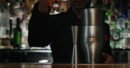 Close up of a professional bartender is preparing an alcoholic cocktail with ice cubes in a shaker