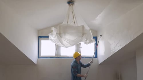 A Man Paints a Wall with a Roller Makes Repairs in the Room of the Attic Floor