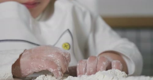 Porträt eines kleinen Mädchens in der Küche, verkleidet als professionelle Köchin, spielt mit Mehl, bekommt h