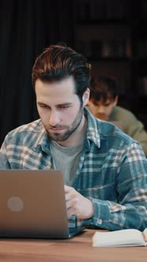 Millennial Male Student Engaged in Work on Laptop at Library