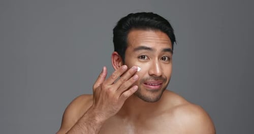 Face, cream and man with skincare, dermatology and beauty with glow on a grey studio background