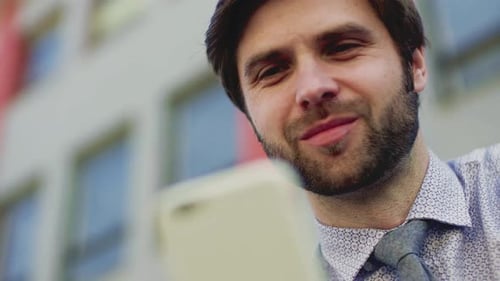 Jeune homme d'affaires avec smartphone assis à l'extérieur en ville, envoyant des SMS. Gros plan