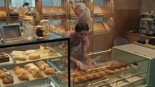 Woman Putting Pastry on Display Shelf in Bakery