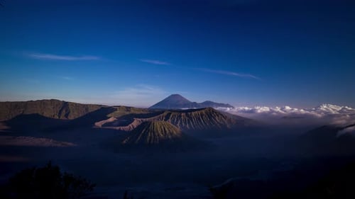 Sunset over the Iconin Mount Bromo, Indonesia, with rolling clouds and puffs coming from the rear vo