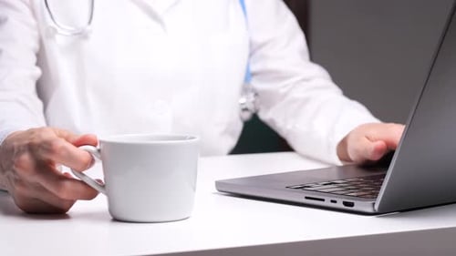 Doctor Typing on Laptop with Coffee Cup