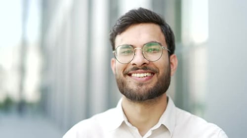 Portrait of smiling businessman in glasses standing on city street near office building. Happy beard