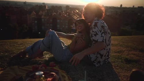 Happy young couple enjoying a romantic date, sitting on the grass in a park and hugging while admiri