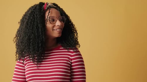 Smiling woman looking towards advertising mockup on yellow background in studio