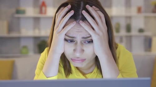 Angry businesswoman sitting at desk working from home on laptop feeling frustrated.