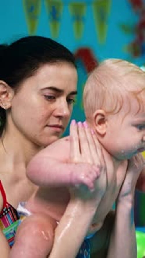 Healthy gymnastics in the water for baby boy. Female coach deeps the kid into the swimming pool.