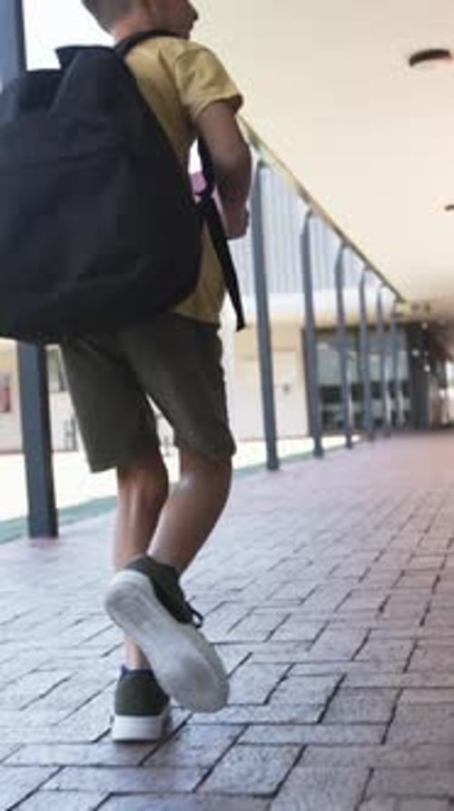 Vídeo vertical: Llevando una mochila y sujetando cuadernos, niño caminando a la escuela