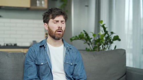 Sick bearded man suffers from seasonal allergies blowing running nose sneezing and coughing sitting