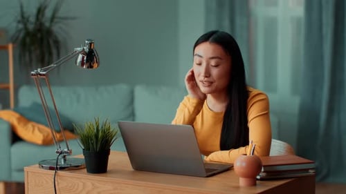 Young Asian Woman Engages in Online Conversation From a Cozy Home Office
