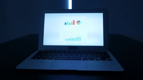Laptop Displaying Data Graphs in Dark Blue Environment