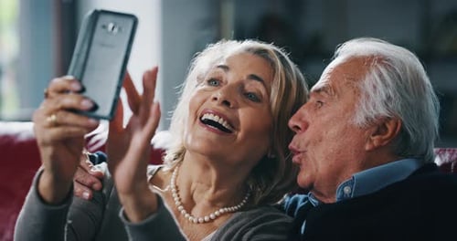 Close up of happy mature senior couple is taking selfie with a smartphone in living room.