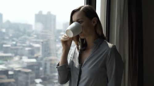 Young Woman Drinking Coffee and Admire View From Window at Home 30s