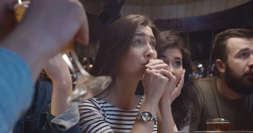 Girls and Guys Fans of Soccer Watching Match Together at Night in Pub and Worrying for Their