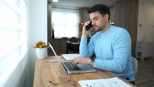 Working remotely in a cozy home office while multitasking with a phone call and laptop usage