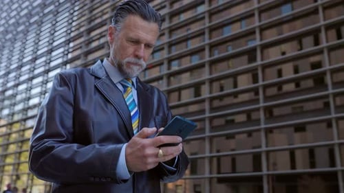 Mature Businessman Using Mobile Phone App Walking in City Street