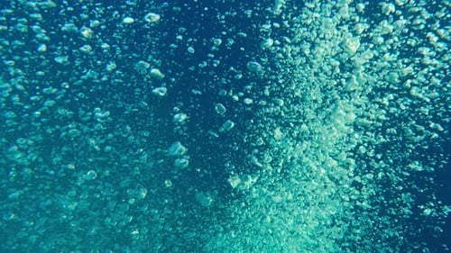 Top view of motion of air bubbles popping up to surface against deep blue sea