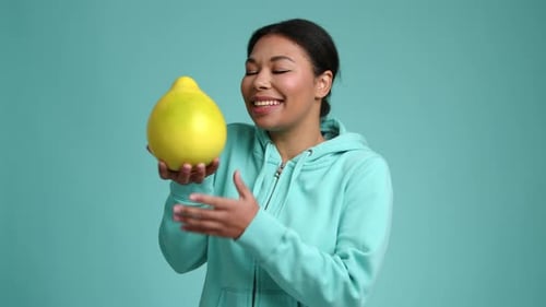 Woman Holds and Smells Large Yellow Citrus Fruit