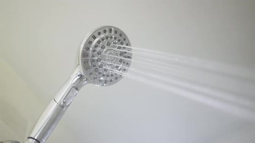 Male hand flips a switch on the running shower head to switch between the different jet settings. Cl