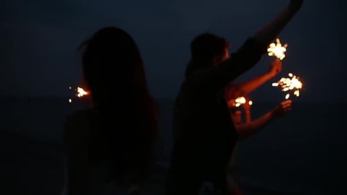 Amigos caminhando, dançando e se divertindo durante a festa noturna à beira-mar com luzes cintilantes de Bengala