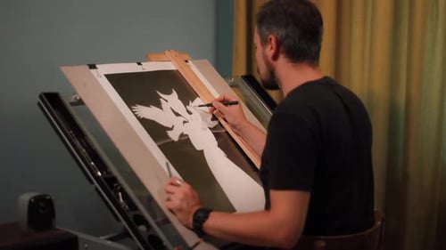 Tracking shot of a pencil artist at his table drawing a woman's portrait