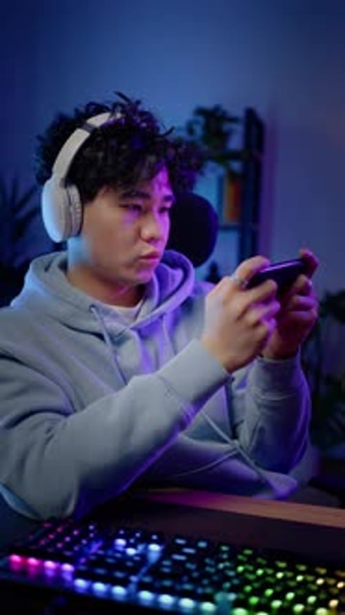 Young Man Playing Mobile Game in Blue Lit Room