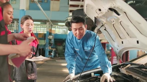 Supervisor engineer is teaching mechanic workers about car repair at a garage.