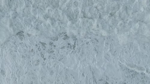 Aerial Video Towering Storm Waves Crash with Swirling Foam Patterns Along the Scenic Sandy Beach