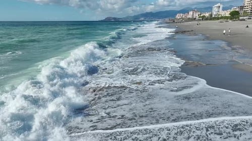 Aerial Video Crashing Storm Waves and Swirling Foam Patterns Transform the Scenic Sandy Beach