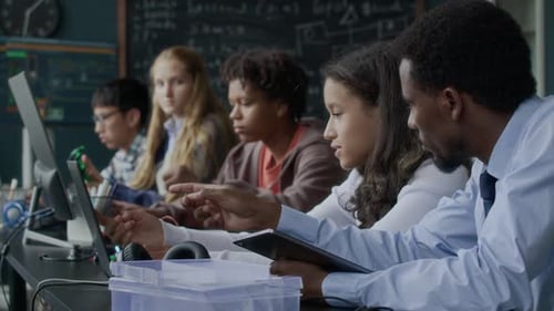 Teacher Helping Students with Computers in Classroom