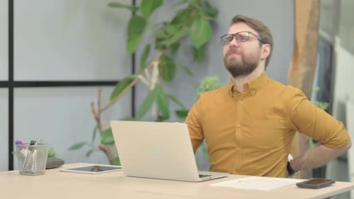Young Adult Massaging Lower Back Pain While Using Laptop