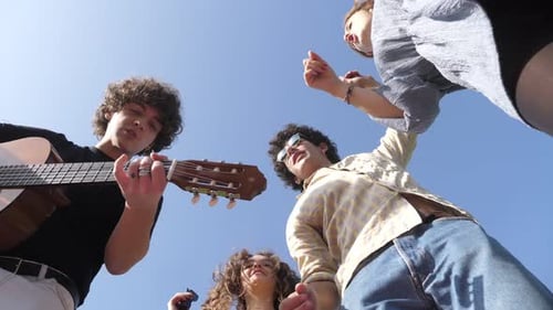 portrait of young happy friends at park playing guitar, singing and dancing