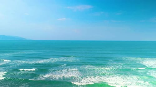 Ocean Waves Rolling Onto Sandy Shoreline Bright Azure Sky Overhead Distant Coastline Blurring Into