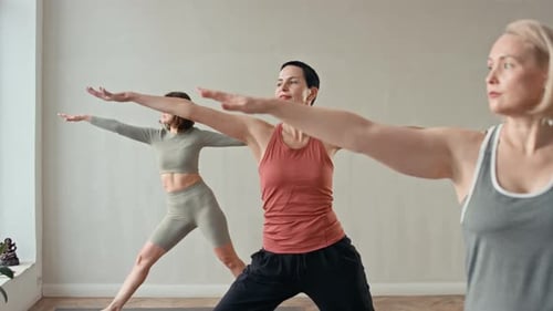 Tres mujeres haciendo la postura de Virabhadrasana II durante la clase de yoga