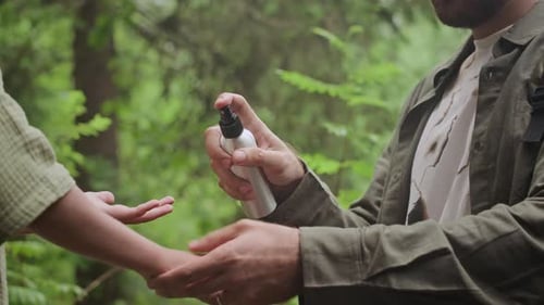 Adult Sprays Bug Repellent on Child in Forest