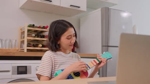 Woman Playing Ukulele at Table Indoors