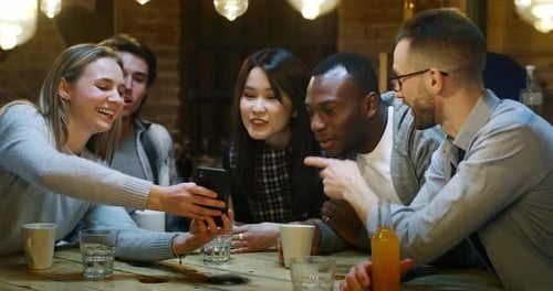 Slow motion of smiling friends having coffee at cafe and having fun with mobile cell phone. Shot i