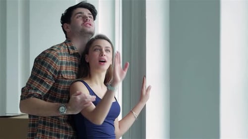Joyful Couple in Love Gazing Out the Window Surrounded By Moving Boxes