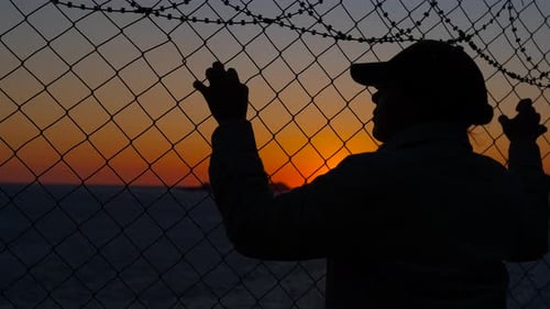 Silhouette Leans on Barbed Wire Fence at Sunset
